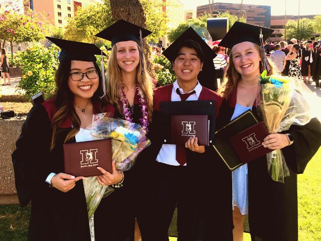 Four students posing for the picture with diplomas on graduation day.