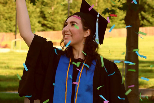 A happy female student in black cap and gown celebrates on her graduation day.