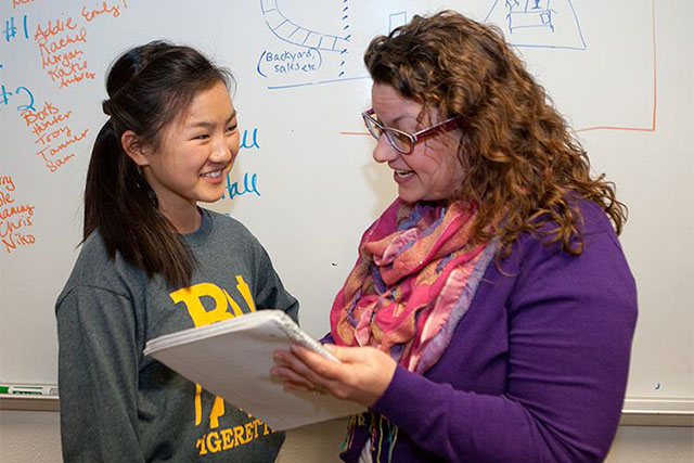 A female student is asking the teacher some questions in front of the white board in the classroom.