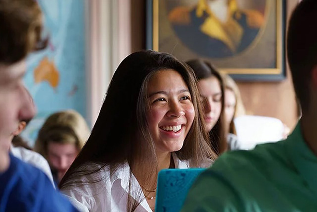 A smiling female student sitting in classroom together with her classmates.